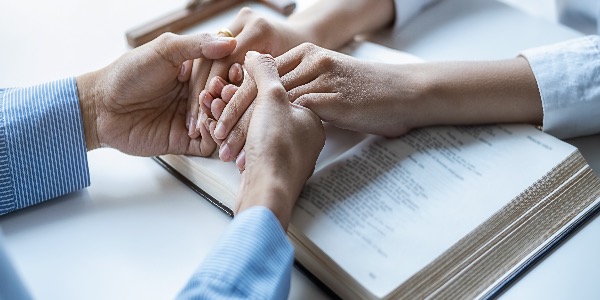 2 christenen houden elkaars hand vast boven een opengeslagen Bijbel